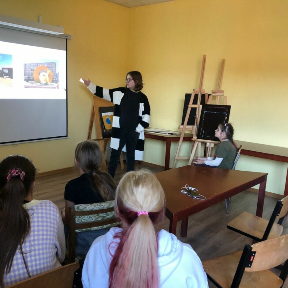 Skolnieces prezentē prezentāciju, stāstot par pieredzēto nometnē Rumānijā