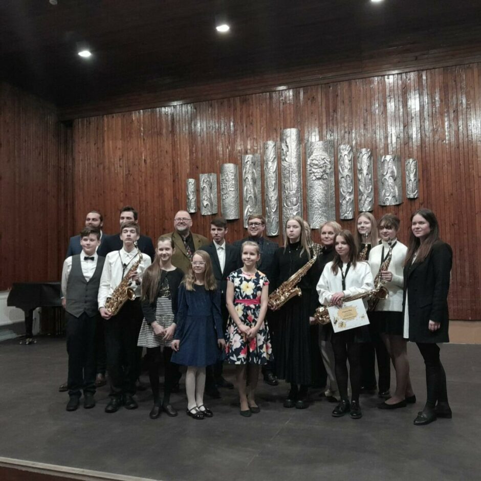 Saksofonu sadraudzības pasākuma dalībnieku un pedagogu kopbilde Jelgavas Mūzikas vidusskolas zālē