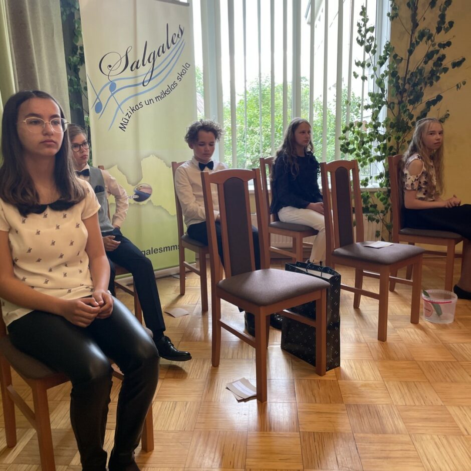 Absolventi sēž savos krēslos, kamēr kādu no absolventiem sveic izlaidumā