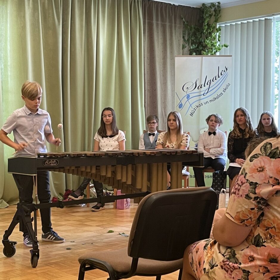5. klases sitaminstrumentu audzēknis spēlē marimbu izlaidumā kā apsveikumu absolventiem